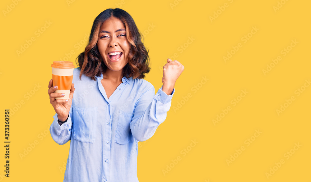 Young beautiful mixed race woman drinking a coffee from take away cup screaming proud, celebrating victory and success very excited with raised arms Young beautiful mixed race woman drinking a coffee from take away cup screaming proud, celebrating victory and success very excited with raised arms