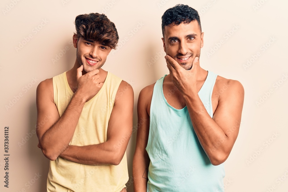 Young gay couple wearing casual clothes looking confident at the camera smiling with crossed arms and hand raised on chin. thinking positive.