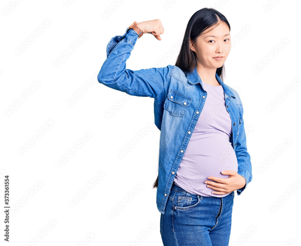 Young beautiful chinese woman pregnant expecting baby strong person showing arm muscle, confident and proud of power Young beautiful chinese woman pregnant expecting baby strong person showing arm muscle, confident and proud of power