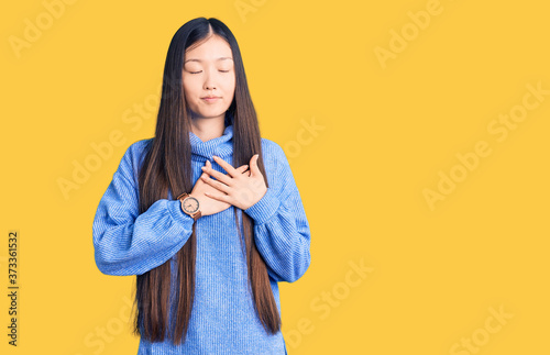 Young beautiful chinese woman wearing casual turtleneck sweater smiling with hands on chest with closed eyes and grateful gesture on face. health concept. © Krakenimages.com