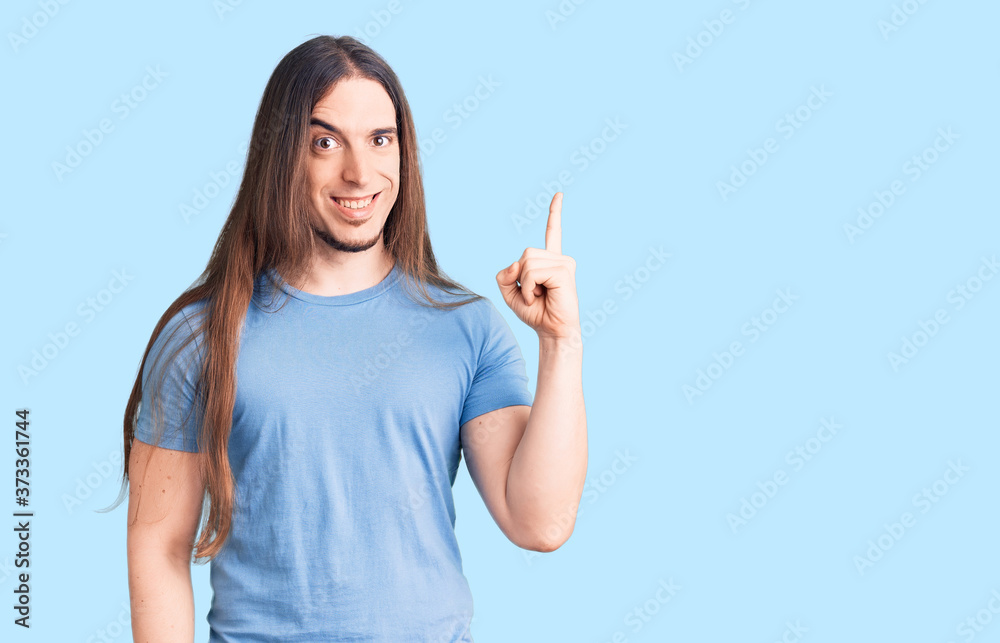Young adult man with long hair wearing casual clothes pointing finger up with successful idea. exited and happy. number one.