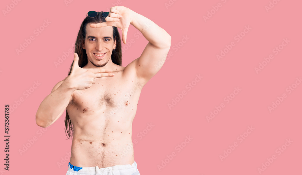 Young adult man with long hair wearing swimwear shirtless smiling making frame with hands and fingers with happy face. creativity and photography concept. Young adult man with long hair wearing swimwear shirtless smiling making frame with hands and fingers with happy face. creativity and photography concept.