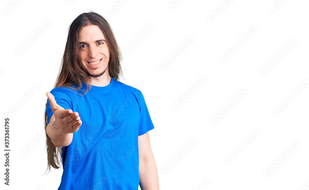 Young adult man with long hair wearing swimwear smiling friendly offering handshake as greeting and welcoming. successful business. Young adult man with long hair wearing swimwear smiling friendly offering handshake as greeting and welcoming. successful business.