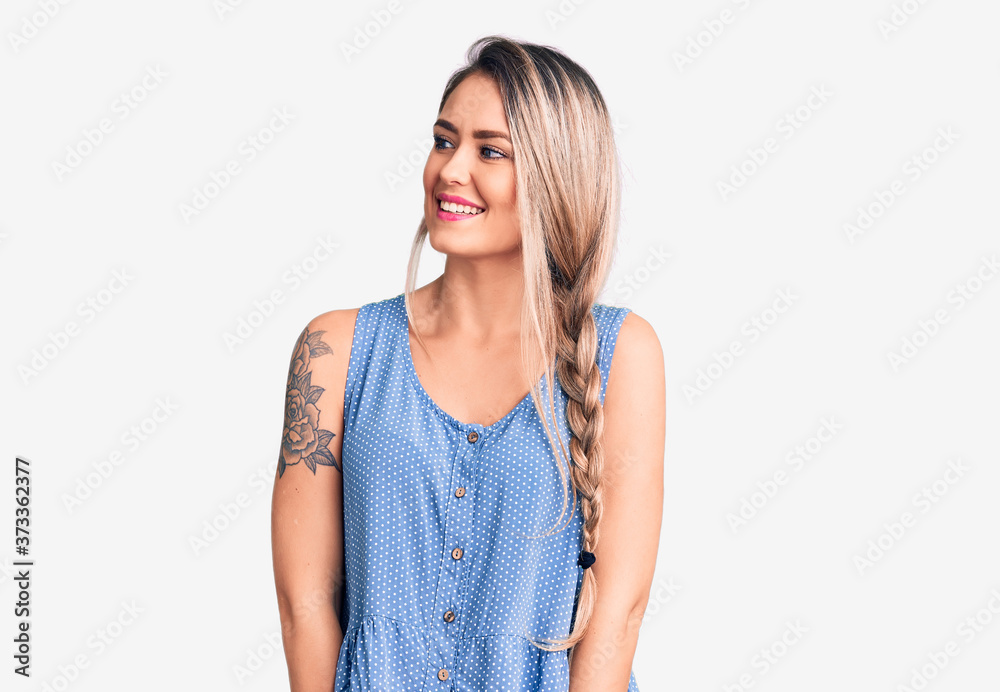 Young beautiful blonde woman wearing casual sleeveless t-shirt looking away to side with smile on face, natural expression. laughing confident. Young beautiful blonde woman wearing casual sleeveless t-shirt looking away to side with smile on face, natural expression. laughing confident.