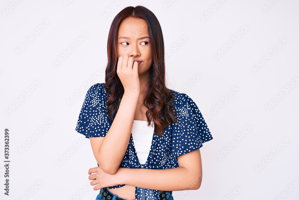 Young beautiful chinese girl wearing casual clothes looking stressed and nervous with hands on mouth biting nails. anxiety problem. Young beautiful chinese girl wearing casual clothes looking stressed and nervous with hands on mouth biting nails. anxiety problem.
