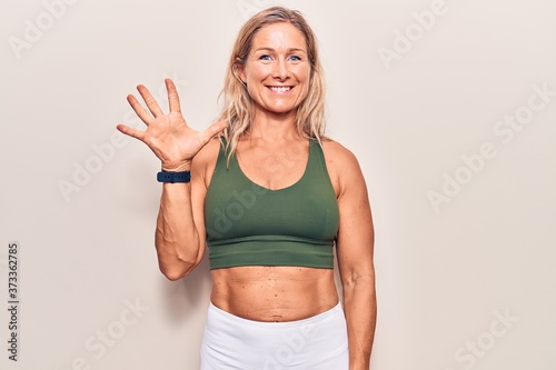 Middle age caucasian blonde woman wearing sportswear showing and pointing up with fingers number five while smiling confident and happy. © Krakenimages.com