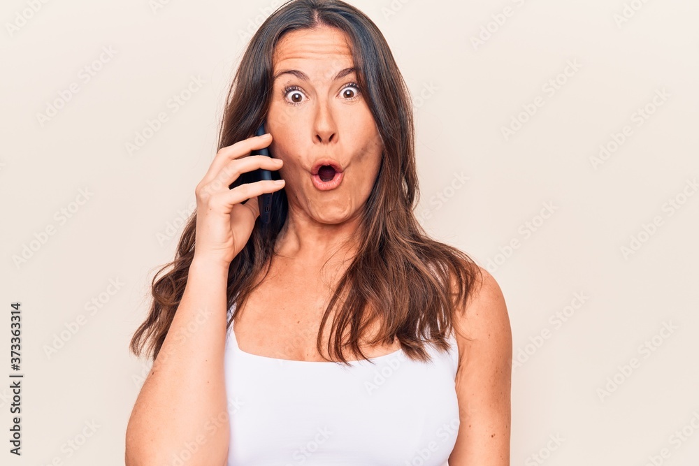 Beautiful brunette woman having conversation talking on the smartphone over white background scared and amazed with open mouth for surprise, disbelief face Beautiful brunette woman having conversation talking on the smartphone over white background scared and amazed with open mouth for surprise, disbelief face