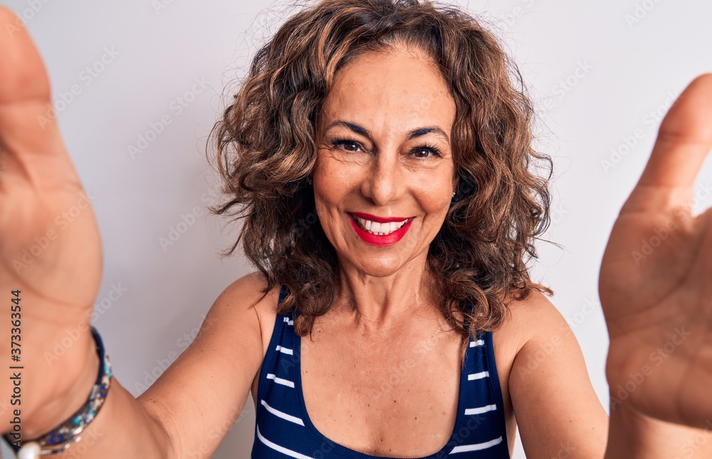 Middle age beautiful brunette woman wearing striped t-shirt standing over white background looking at the camera smiling with open arms for hug. Cheerful expression embracing happiness. Middle age beautiful brunette woman wearing striped t-shirt standing over white background looking at the camera smiling with open arms for hug. Cheerful expression embracing happiness.
