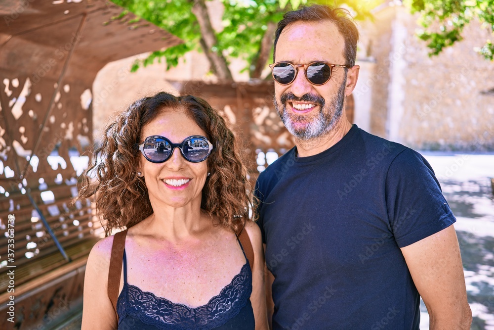 Middle age beautiful couple wearing casual clothes and sunglasses smiling happy. Standing with smile on face hugging at town street. Middle age beautiful couple wearing casual clothes and sunglasses smiling happy. Standing with smile on face hugging at town street.