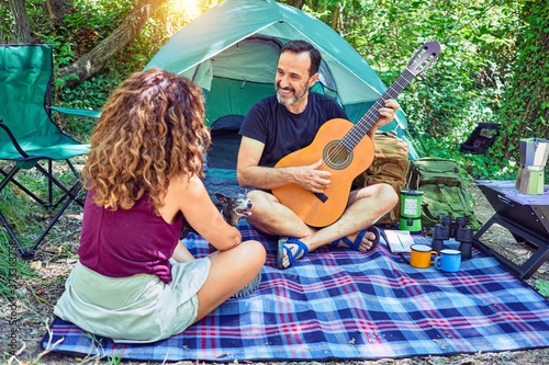 Middle age couple of hiker smiling happy camping at the forest. Sitting on the floor singing song playing classical guitar