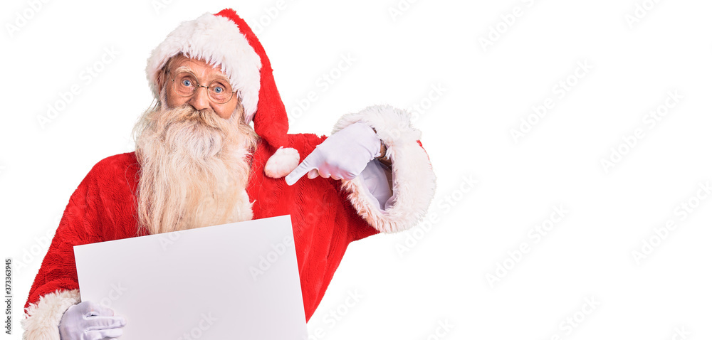 Old senior man with grey hair and long beard wearing santa claus costume holding banner pointing finger to one self smiling happy and proud Old senior man with grey hair and long beard wearing santa claus costume holding banner pointing finger to one self smiling happy and proud