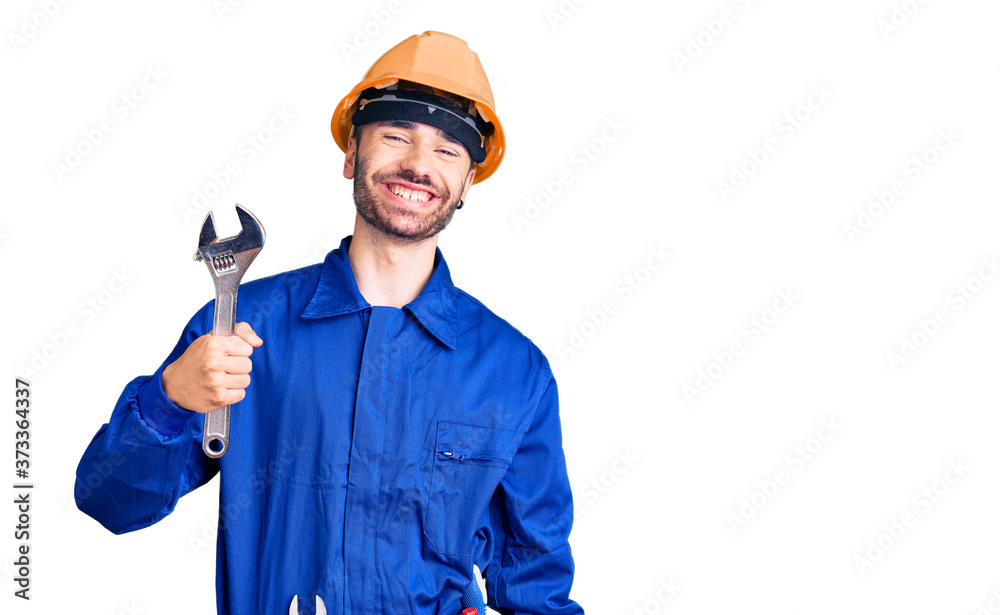 Young hispanic man wearing electrician uniform holding wrench looking positive and happy standing and smiling with a confident smile showing teeth Young hispanic man wearing electrician uniform holding wrench looking positive and happy standing and smiling with a confident smile showing teeth