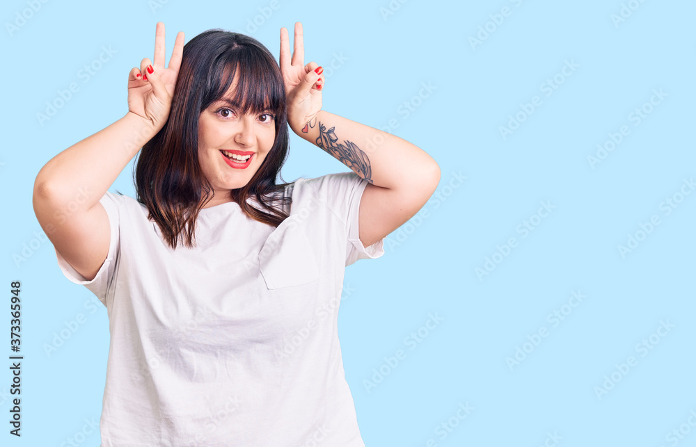 Fototapeta premium Young plus size woman wearing casual clothes posing funny and crazy with fingers on head as bunny ears, smiling cheerful