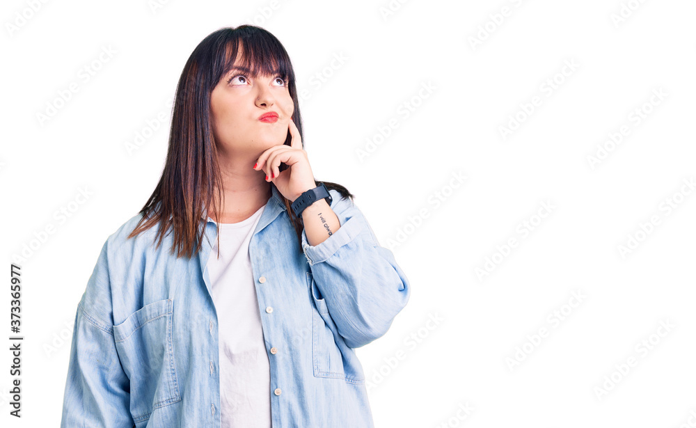 Young plus size woman wearing casual clothes serious face thinking about question with hand on chin, thoughtful about confusing idea Young plus size woman wearing casual clothes serious face thinking about question with hand on chin, thoughtful about confusing idea