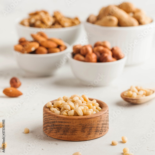 A handful of pine nuts in a wooden bowl, assorted nuts on a light background. Healthy snacks, healthy fats.