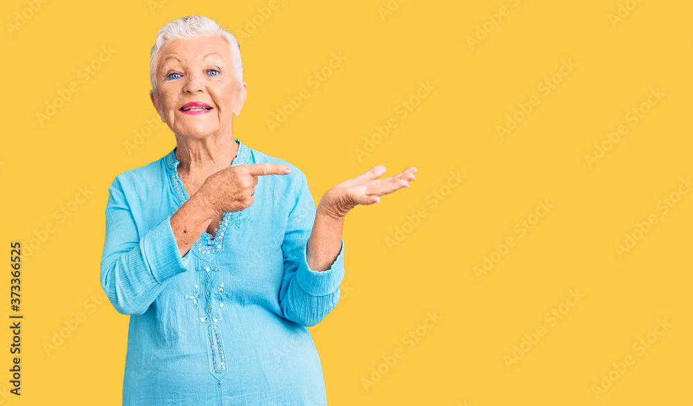 Senior beautiful woman with blue eyes and grey hair wearing summer dress amazed and smiling to the camera while presenting with hand and pointing with finger. Senior beautiful woman with blue eyes and grey hair wearing summer dress amazed and smiling to the camera while presenting with hand and pointing with finger.