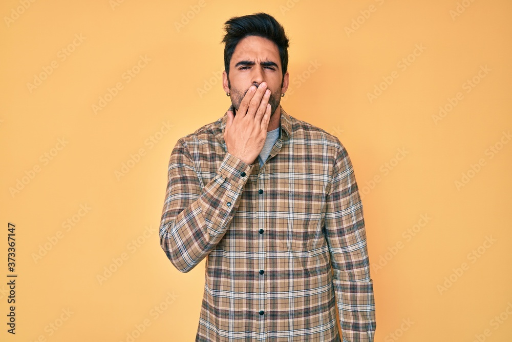 Handsome hispanic man with beard wearing casual clothes bored yawning tired covering mouth with hand. restless and sleepiness.