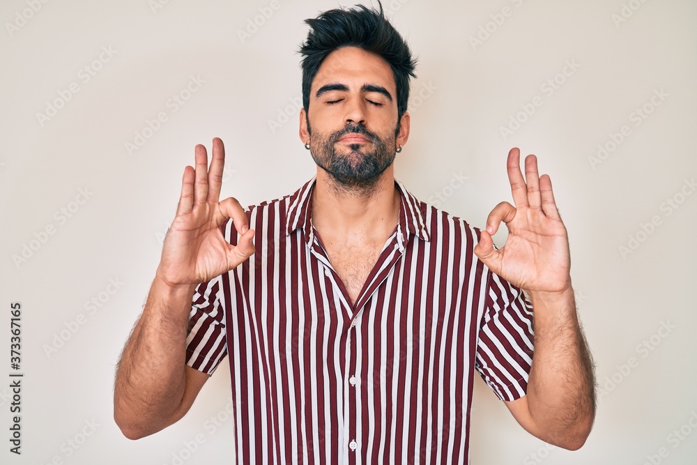 Naklejka premium Handsome hispanic man with beard wearing casual clothes relax and smiling with eyes closed doing meditation gesture with fingers. yoga concept.