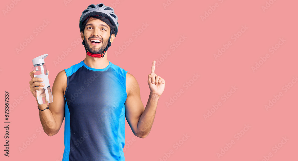 Handsome hispanic man wearing bike helmet and holding water bottle surprised with an idea or question pointing finger with happy face, number one Handsome hispanic man wearing bike helmet and holding water bottle surprised with an idea or question pointing finger with happy face, number one