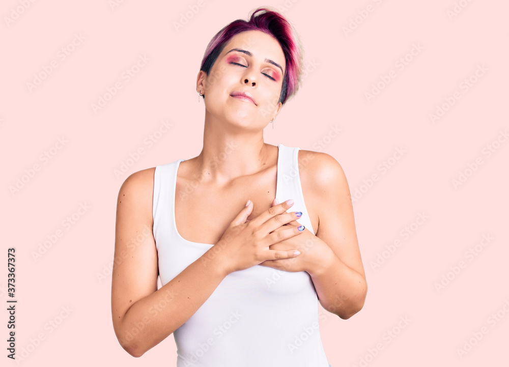 Young beautiful woman with pink hair wearing casual clothes smiling with hands on chest with closed eyes and grateful gesture on face. health concept. Young beautiful woman with pink hair wearing casual clothes smiling with hands on chest with closed eyes and grateful gesture on face. health concept.
