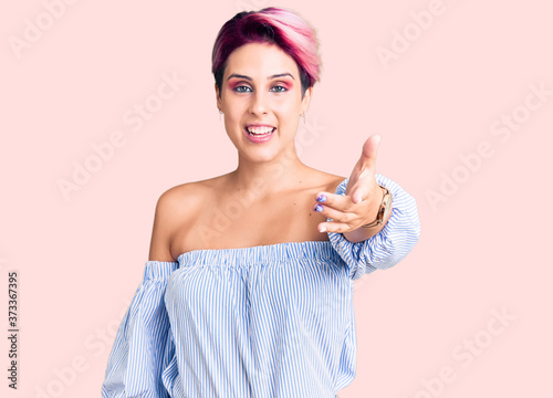 Young beautiful woman with pink hair wearing casual clothes smiling friendly offering handshake as greeting and welcoming. successful business.