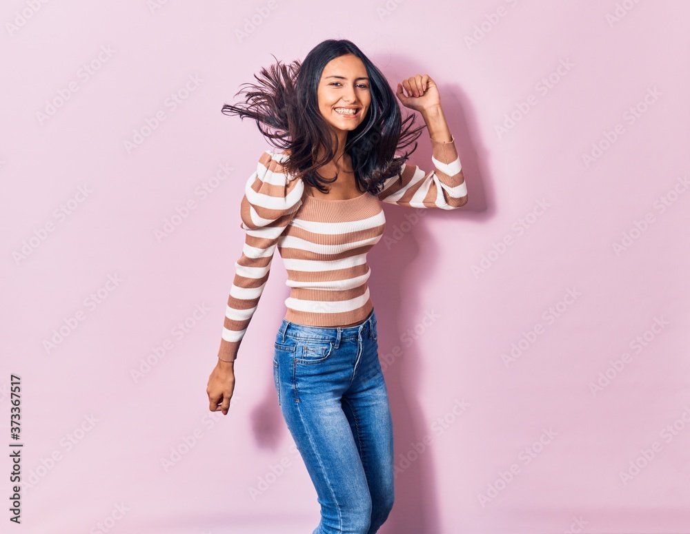 Young beautiful latin woman wearing casual clothes smiling happy. Jumping with smile on face over isolated pink background Young beautiful latin woman wearing casual clothes smiling happy. Jumping with smile on face over isolated pink background