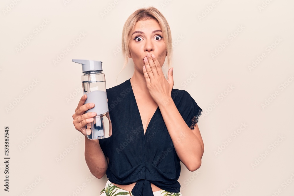 Young beautiful blonde woman drinking bottle of water over isolated white background covering mouth with hand, shocked and afraid for mistake. Surprised expression Young beautiful blonde woman drinking bottle of water over isolated white background covering mouth with hand, shocked and afraid for mistake. Surprised expression