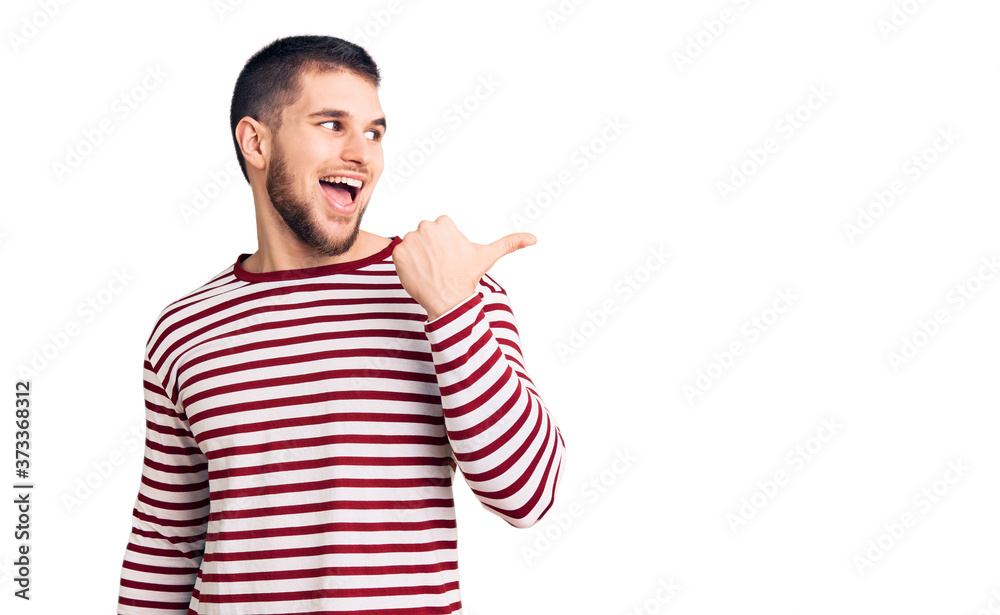 Naklejka premium Young handsome man wearing striped sweater smiling with happy face looking and pointing to the side with thumb up.