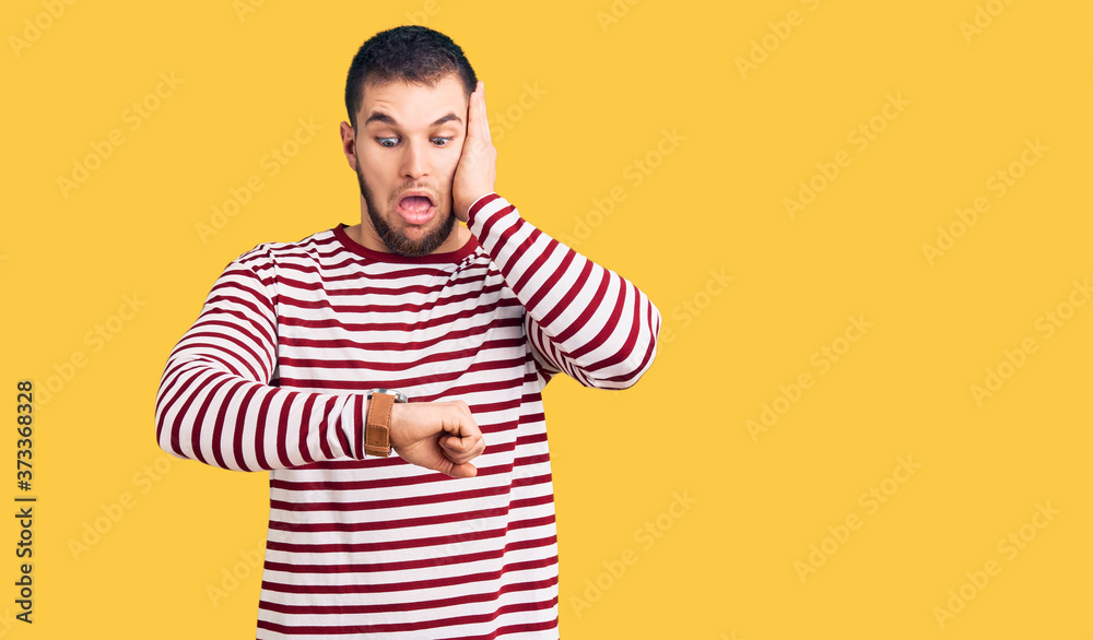Young handsome man wearing striped sweater looking at the watch time worried, afraid of getting late Young handsome man wearing striped sweater looking at the watch time worried, afraid of getting late