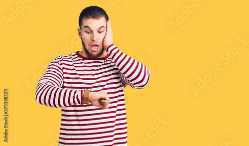 Young handsome man wearing striped sweater looking at the watch time worried, afraid of getting late © Krakenimages.com