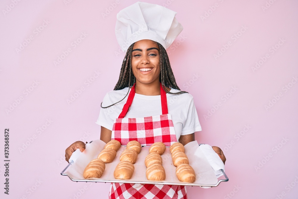Young african american woman with braids wearing baker uniform holding homemade bread smiling and laughing hard out loud because funny crazy joke. Young african american woman with braids wearing baker uniform holding homemade bread smiling and laughing hard out loud because funny crazy joke.