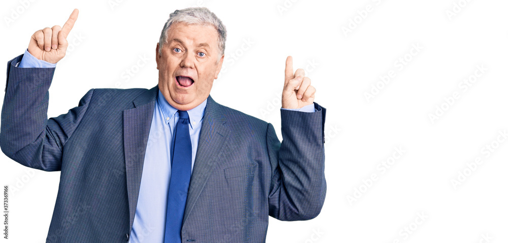 Senior grey-haired man wearing business jacket smiling amazed and surprised and pointing up with fingers and raised arms. Senior grey-haired man wearing business jacket smiling amazed and surprised and pointing up with fingers and raised arms.