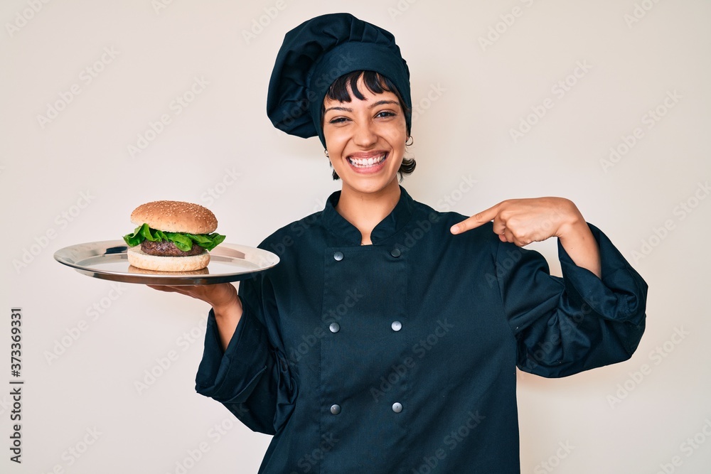 Beautiful brunettte woman chef holding burguer pointing finger to one self smiling happy and proud Beautiful brunettte woman chef holding burguer pointing finger to one self smiling happy and proud