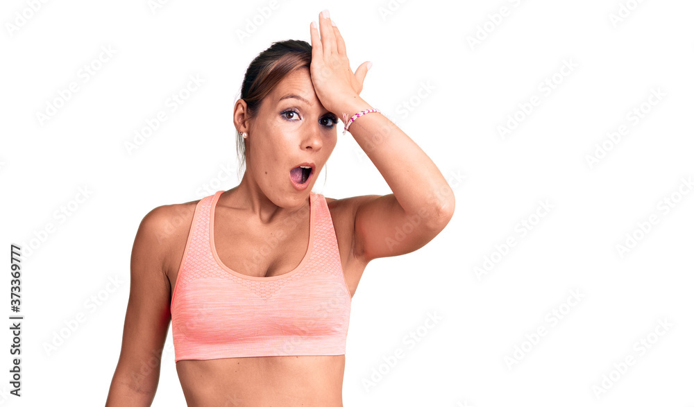 Young beautiful hispanic woman wearing sportswear surprised with hand on head for mistake, remember error. forgot, bad memory concept. Young beautiful hispanic woman wearing sportswear surprised with hand on head for mistake, remember error. forgot, bad memory concept.