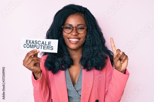 Beautiful african woman holding exascale computers banner smiling with an idea or question pointing finger with happy face, number one photo