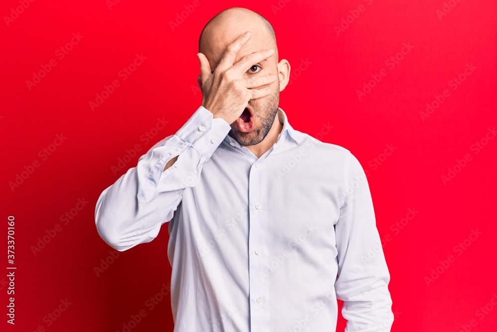 Young handsome bald man wearing elegant shirt peeking in shock covering face and eyes with hand, looking through fingers afraid Young handsome bald man wearing elegant shirt peeking in shock covering face and eyes with hand, looking through fingers afraid
