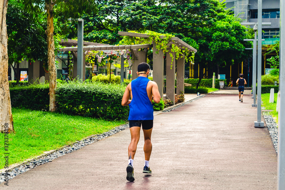 Φωτογραφία A man in a blue singlet and black shorts jogs at a park in the middle of the city
