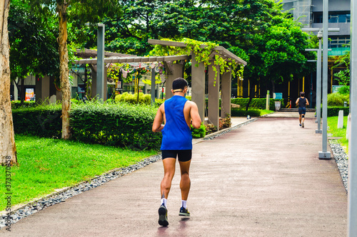 A man in a blue singlet and black shorts jogs at a park in the middle of the city. Morning scene in Fort Bonifacio, Philippines. Back shot, wide angle. photo