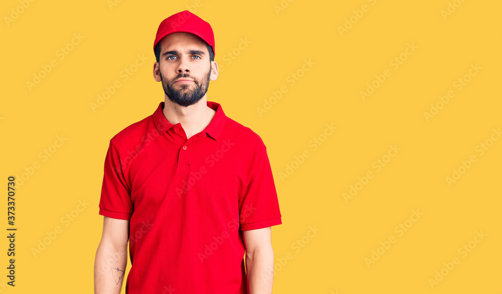 Young handsome man with beard wearing delivery uniform relaxed with serious expression on face. simple and natural looking at the camera.