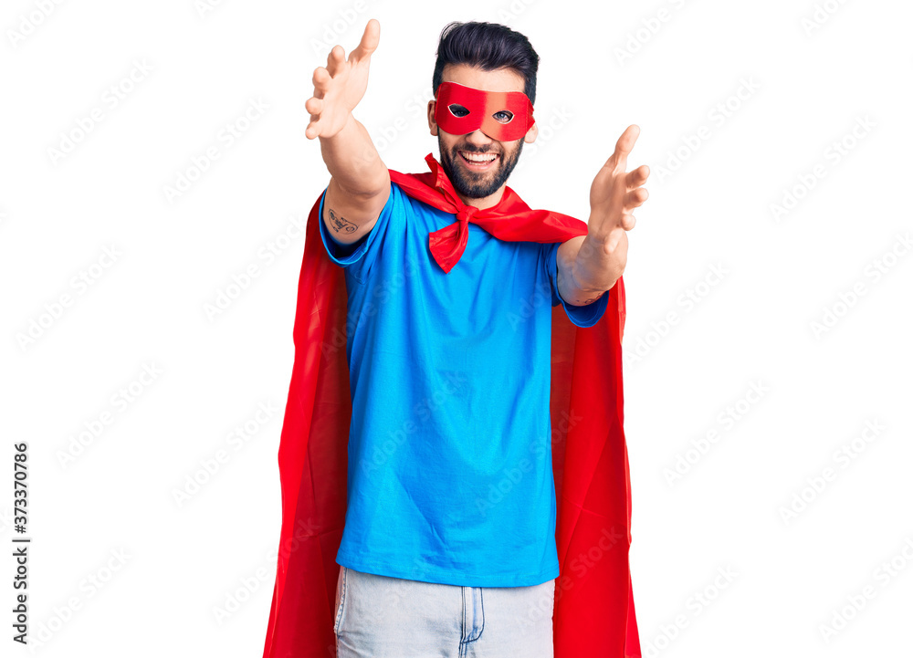 Young handsome man with beard wearing super hero costume looking at the camera smiling with open arms for hug. cheerful expression embracing happiness. Young handsome man with beard wearing super hero costume looking at the camera smiling with open arms for hug. cheerful expression embracing happiness.