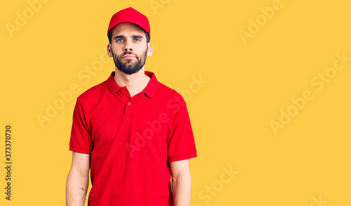 Young handsome man with beard wearing delivery uniform relaxed with serious expression on face. simple and natural looking at the camera.