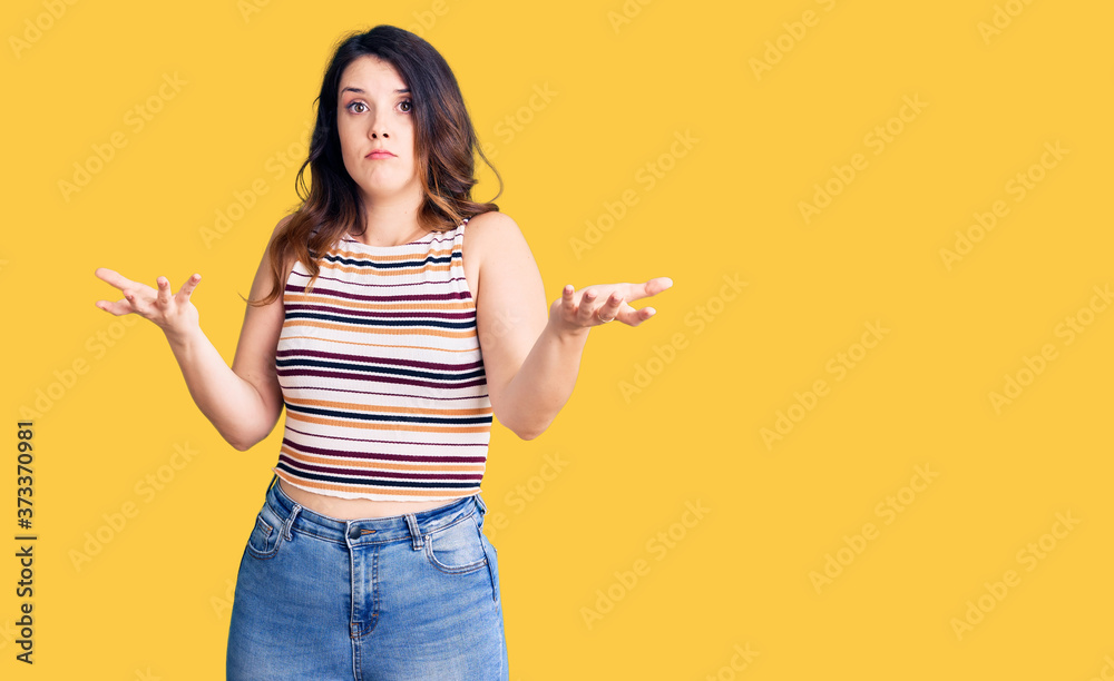 Beautiful young brunette woman wearing casual clothes clueless and confused expression with arms and hands raised. doubt concept. Beautiful young brunette woman wearing casual clothes clueless and confused expression with arms and hands raised. doubt concept.