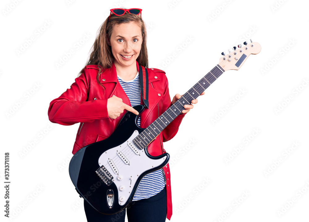 Young beautiful blonde woman playing electric guitar smiling happy pointing with hand and finger