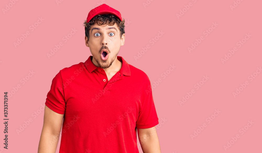 Young handsome man with curly hair wearing delivery uniform scared and amazed with open mouth for surprise, disbelief face Young handsome man with curly hair wearing delivery uniform scared and amazed with open mouth for surprise, disbelief face