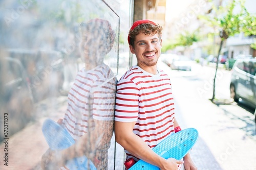 Obraz na plátně Young caucasian skater man smiling happy holding skate leaning on the wall city