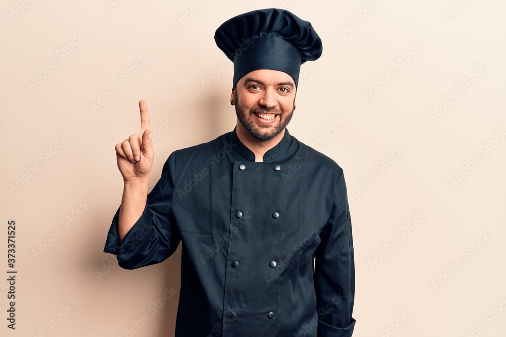 Young hispanic man wearing cooker uniform smiling with an idea or question pointing finger up with happy face, number one Young hispanic man wearing cooker uniform smiling with an idea or question pointing finger up with happy face, number one