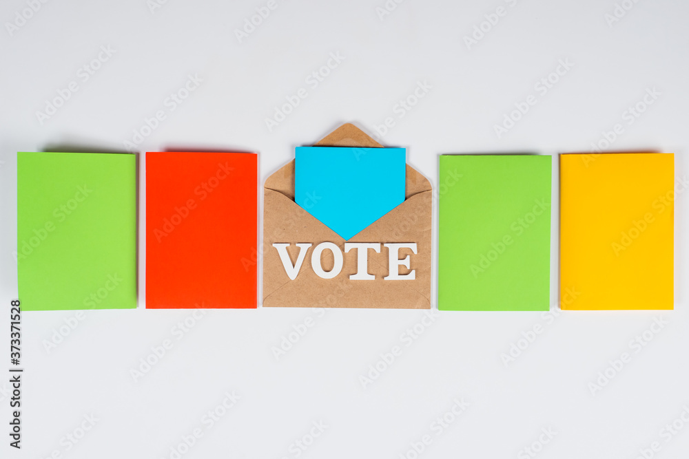 VOTE lettering on craft envelope. Multi-colored papers next to envelope. Concept - sending  ballot by mail. Different colored ballots represent different candidates. Vote absentee in elections.