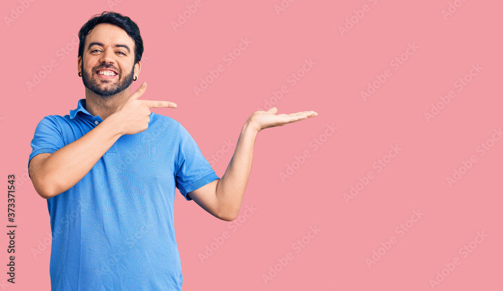 Young hispanic man wearing casual clothes amazed and smiling to the camera while presenting with hand and pointing with finger.