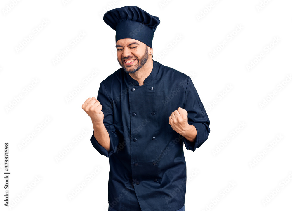 Young hispanic man wearing cooker uniform very happy and excited doing winner gesture with arms raised, smiling and screaming for success. celebration concept.