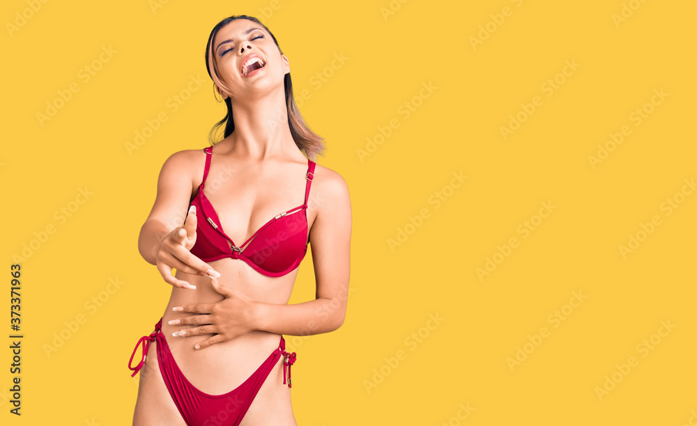Young beautiful woman wearing bikini laughing at you, pointing finger to the camera with hand over body, shame expression Young beautiful woman wearing bikini laughing at you, pointing finger to the camera with hand over body, shame expression